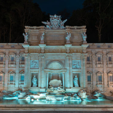 Fontana di Trevi iluminada à noite em Roma, com esculturas clássicas e águas cristalinas em primeiro plano.